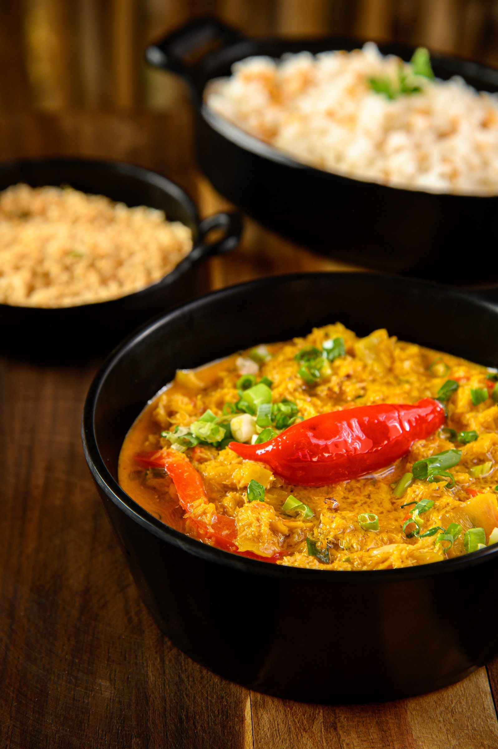 Moqueca de caranguejo com pimenta por cima, arroz e farofa ao fundo
