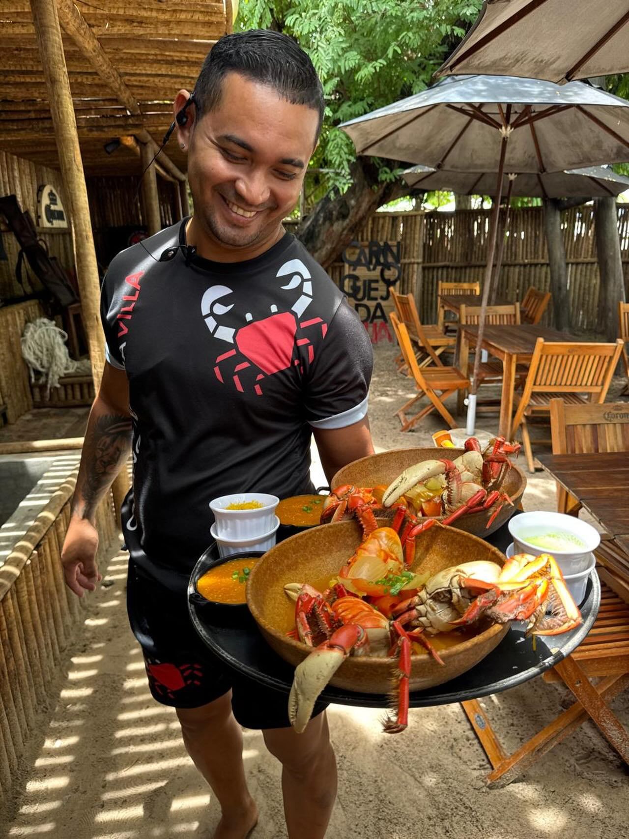 Garçom sorrindo enquanto leva travessas de caranguejo para a mesa
